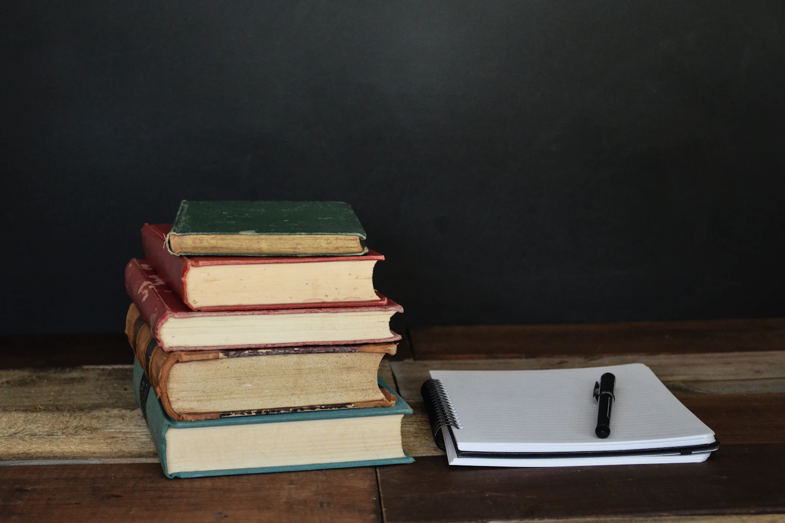 Stapel alter Bücher und ein Notizbuch mit Stift auf einem Holztisch – 4. Semester Zahnmedizin
