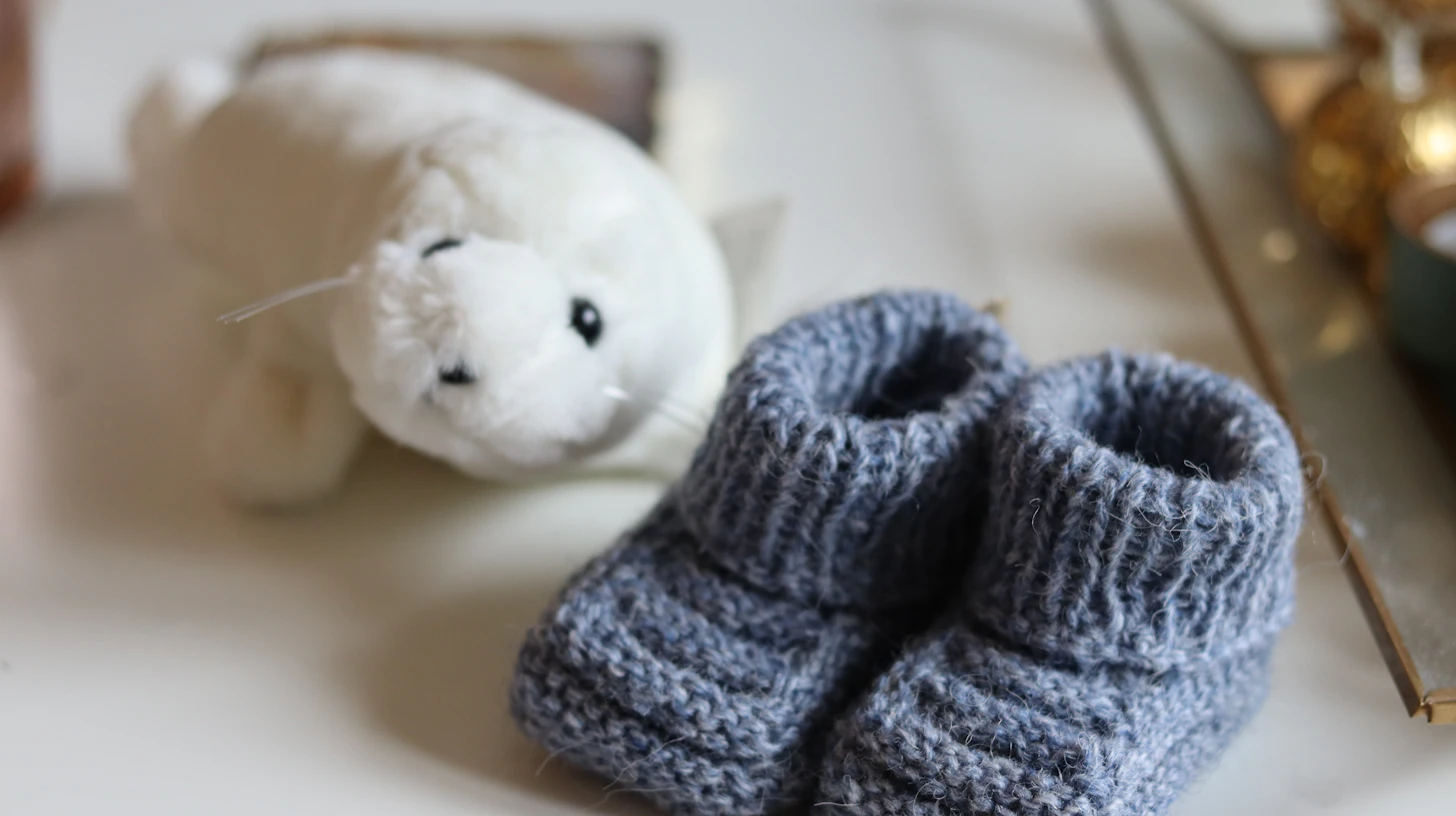 Gestrickte graue Babyschuhe neben einem weißen Kuscheltier – Schwangerschaft und Mutterschutz für Zahnärztinnen
